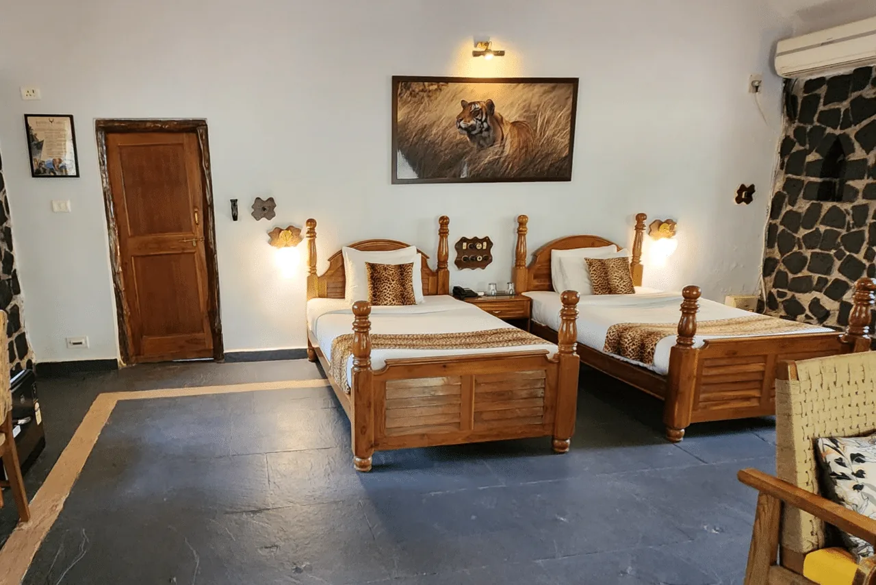 Twin room with a stone feature wall and wooden beds at a luxury jungle resort near Bandhavgarh
